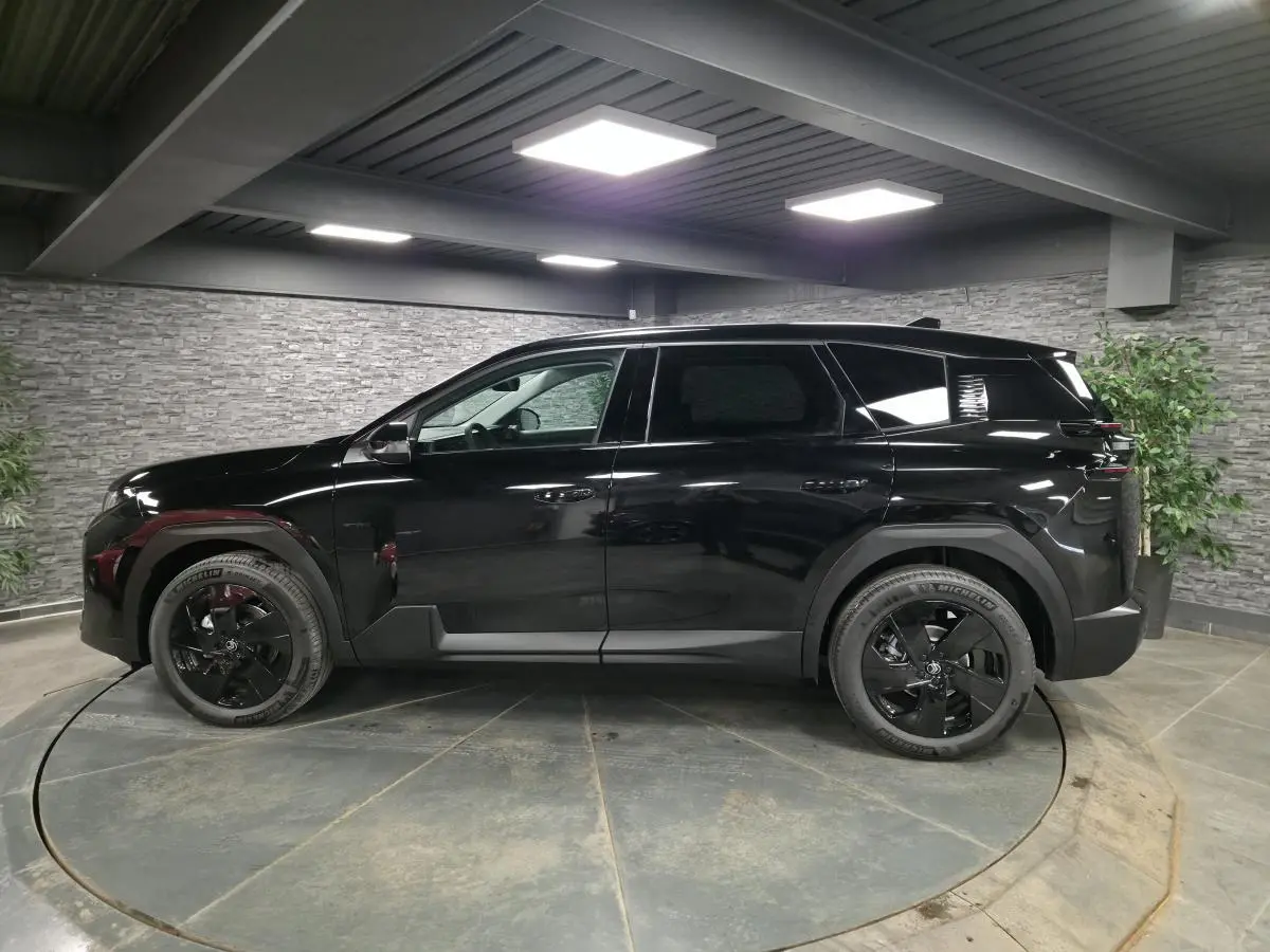 Vue latérale gauche du SUV Citroën C5 Aircross noir brillant avec jantes alliage noires dans un showroom intérieur.