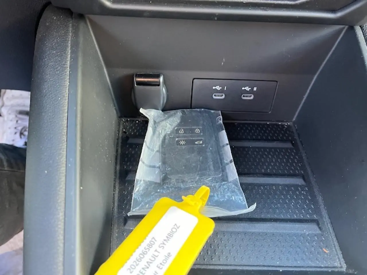 Gros plan sur la console centrale de la Renault Symbioz 2025 avec prises USB-C et clé dans un étui plastique.