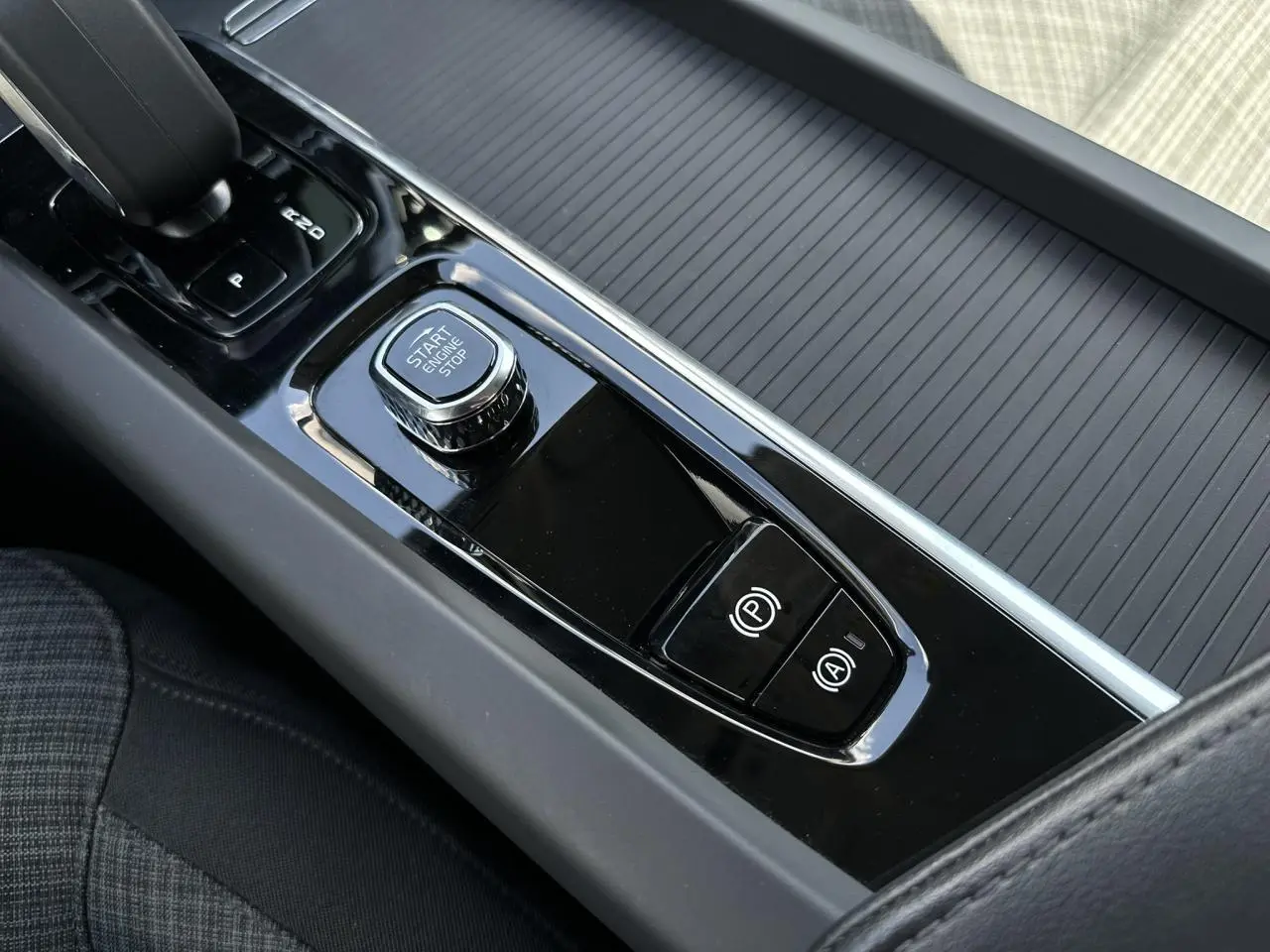 Gros plan sur la console centrale noire brillante de la Volvo S60 B4 197 DCT7 MHEV Core+ avec bouton start/stop et commandes électroniques.