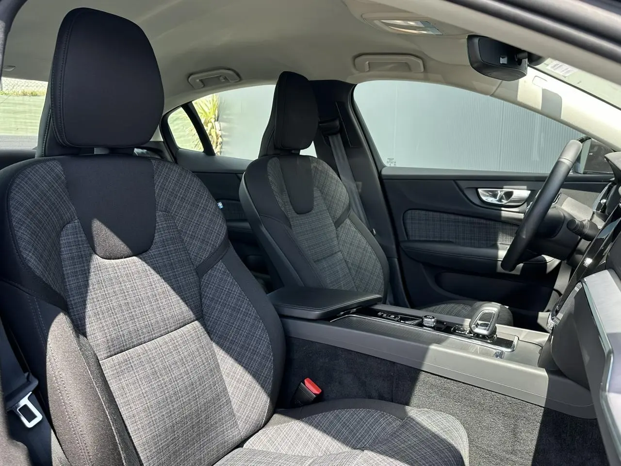 Vue intérieure côté droit du Volvo S60 2024, sièges avant en tissu gris à motif tartan avec console centrale moderne.