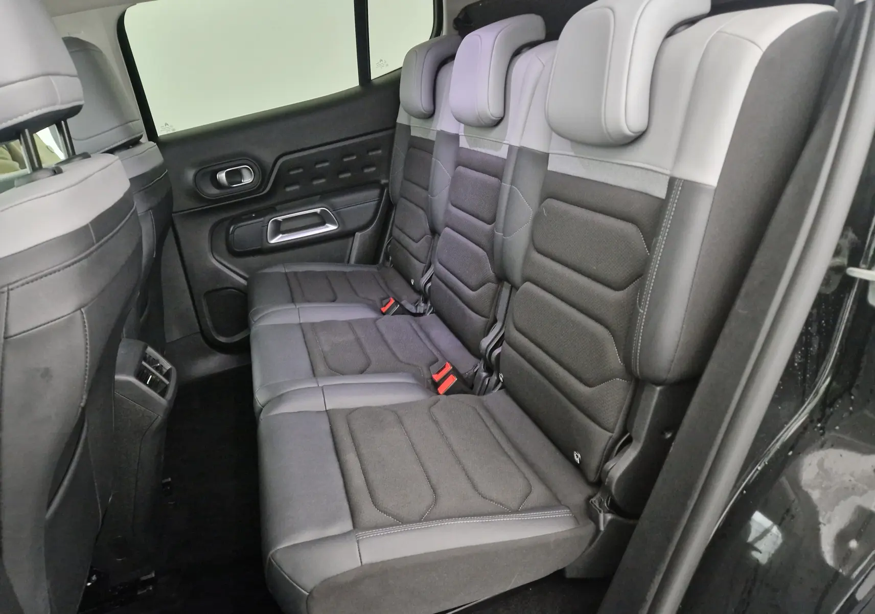 Vue latérale des sièges arrière en tissu et cuir gris foncé du Citroën C5 Aircross noir 2024, avec ceintures rouges visibles.