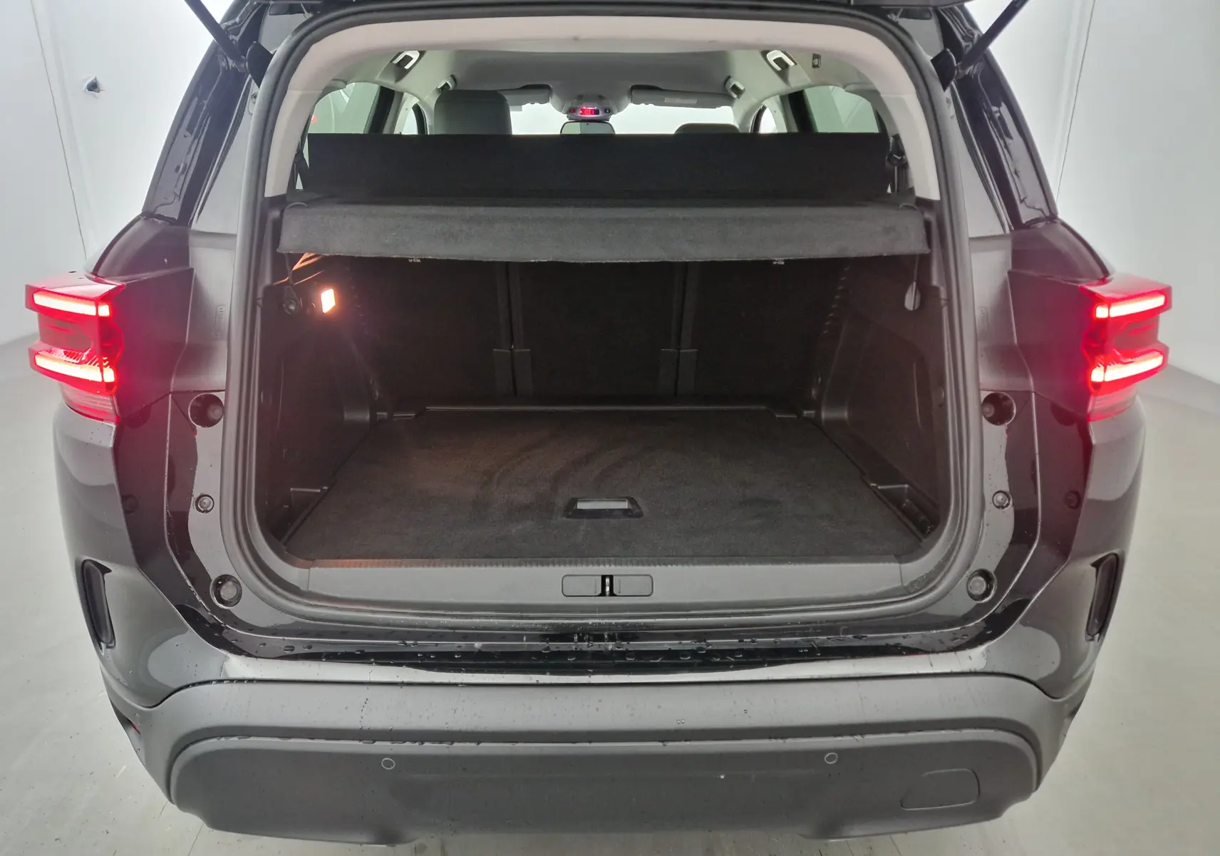 Coffre ouvert vu de l'arrière d'un Citroën C5 Aircross noir 2024 avec feux arrière allumés et cache-bagages en place.