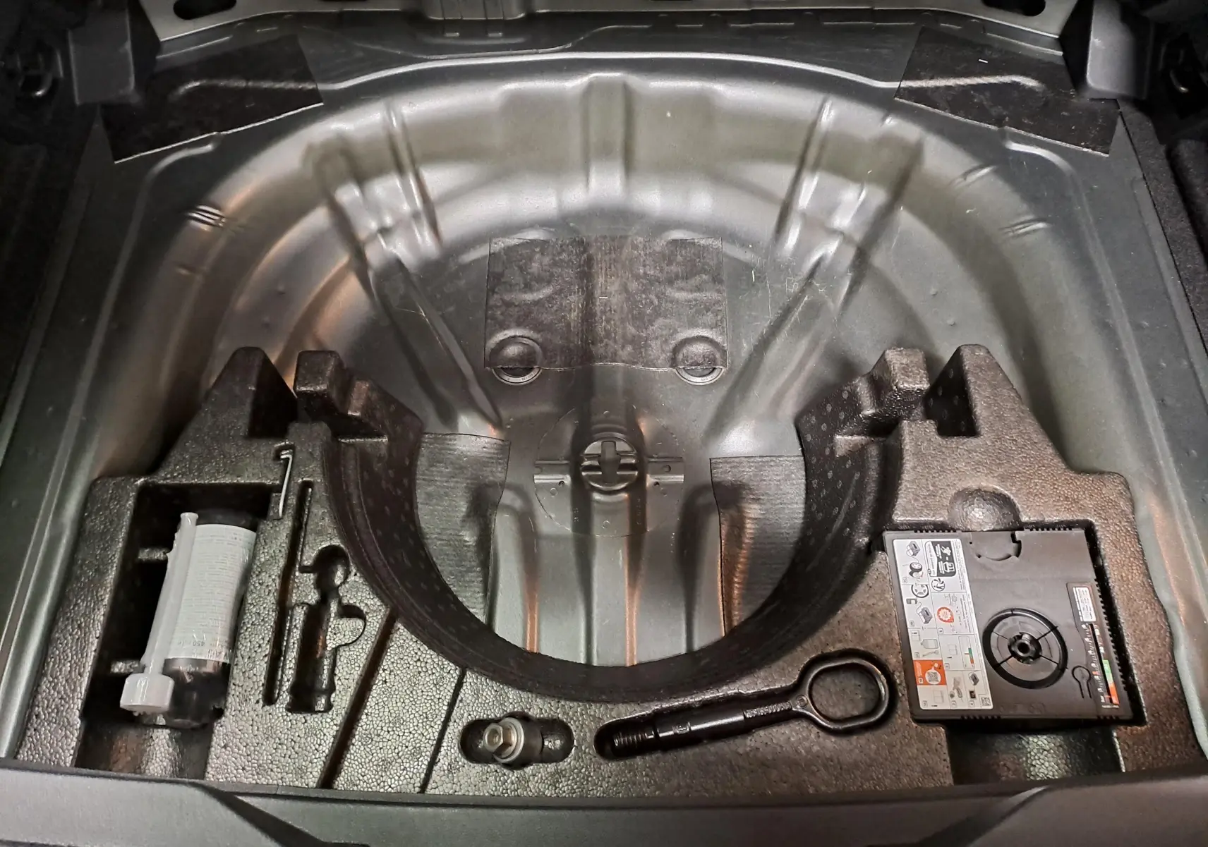 Compartiment de rangement sous le coffre du Volkswagen T-Roc gris Indium, montrant les outils et le kit de réparation pneus.