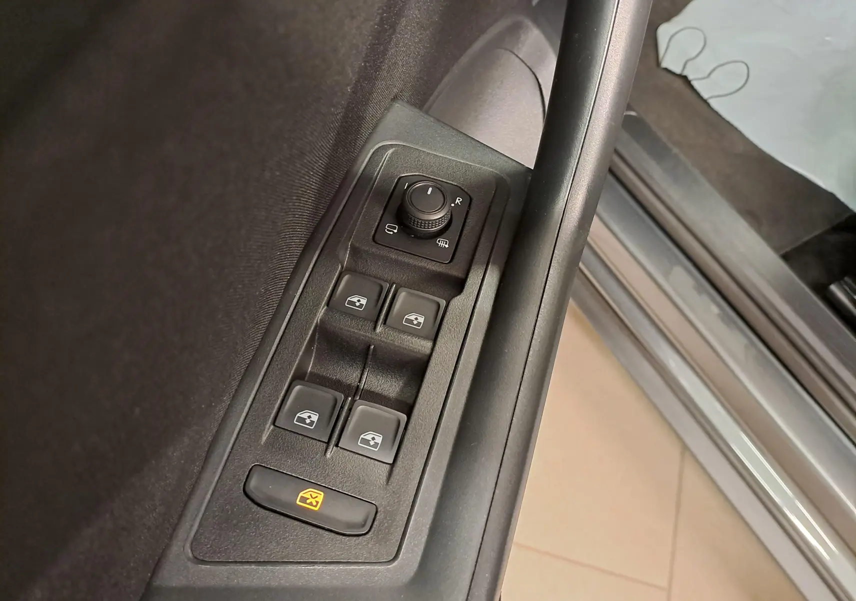 Gros plan sur les commandes des vitres et rétroviseurs côté conducteur du Volkswagen T-Roc gris Indium 2024.