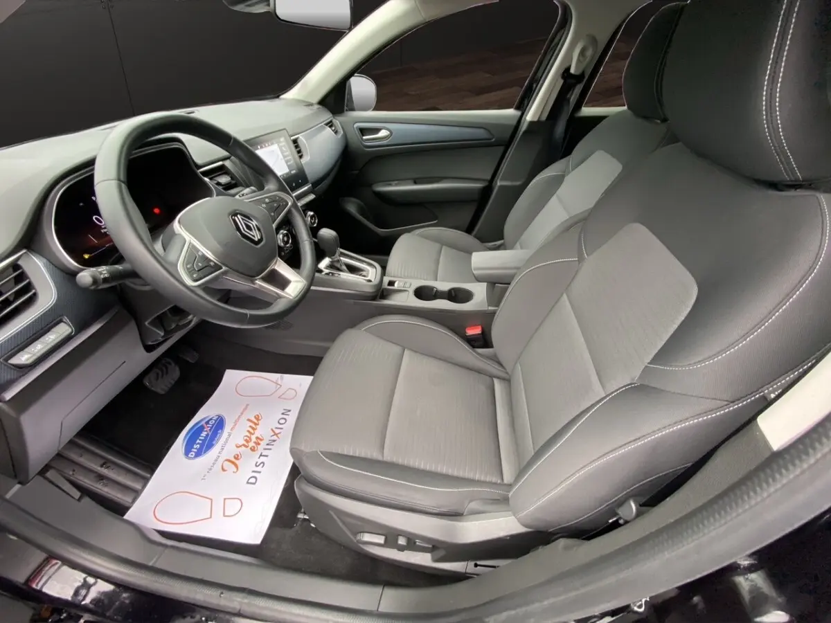 Vue intérieure côté conducteur du Renault Arkana noir 2024, sièges tissu gris et tableau de bord avec écran tactile central.