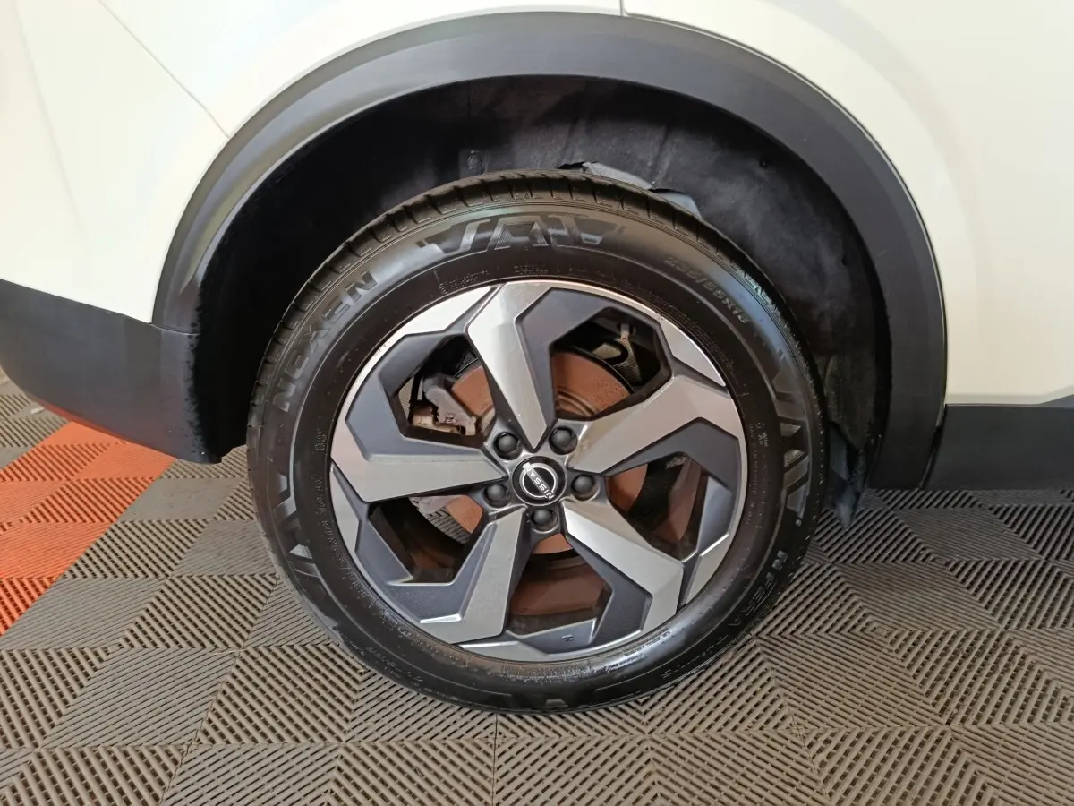 Gros plan sur la roue avant droite du Nissan Qashqai blanc 2024 avec jante alliage gris et logo Nissan au centre.