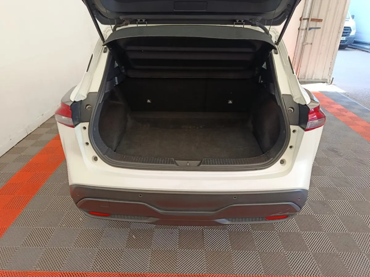 Coffre ouvert vu de l'arrière d'un Nissan Qashqai e-Power blanc, montrant l'espace de chargement vide et tapis noir.