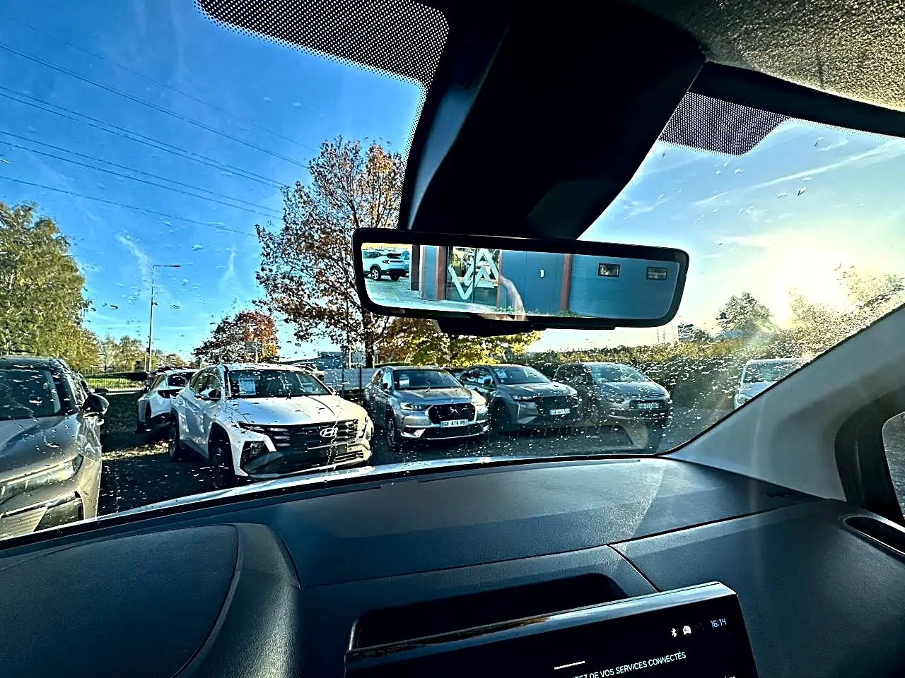 Vue intérieure du pare-brise et rétroviseur d’un Citroën Berlingo blanc, avec plusieurs voitures visibles à l’extérieur.