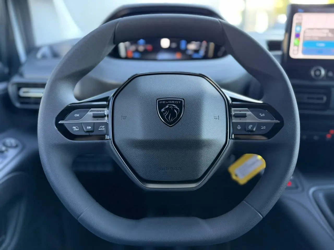 Vue rapprochée du volant multifonctions noir du Peugeot Partner 2026 avec tableau de bord numérique en arrière-plan flou.