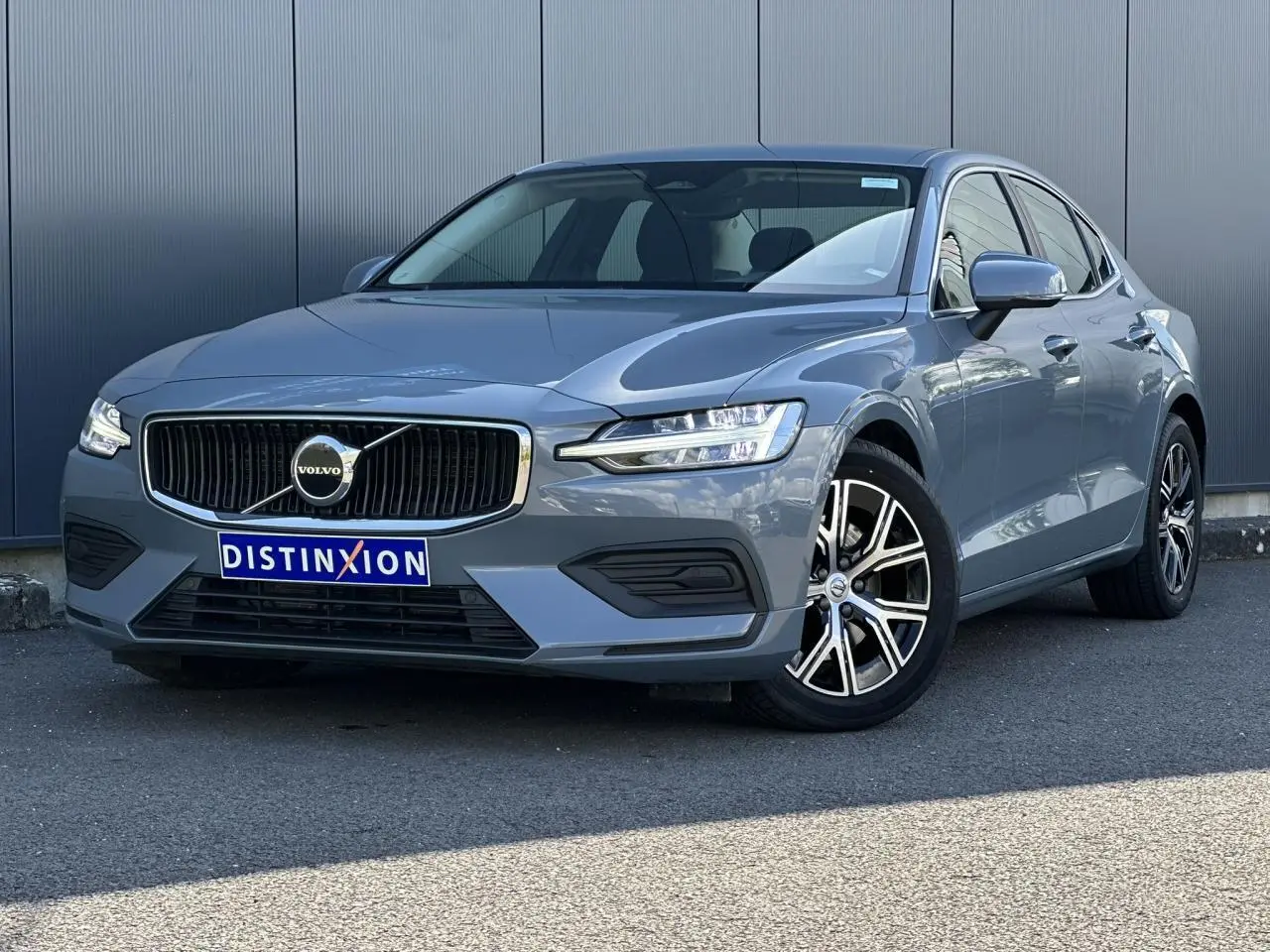 Volvo S60 B4 2024 gris Thunder vue 3/4 avant avec jantes alliage 17 pouces et calandre chromée.