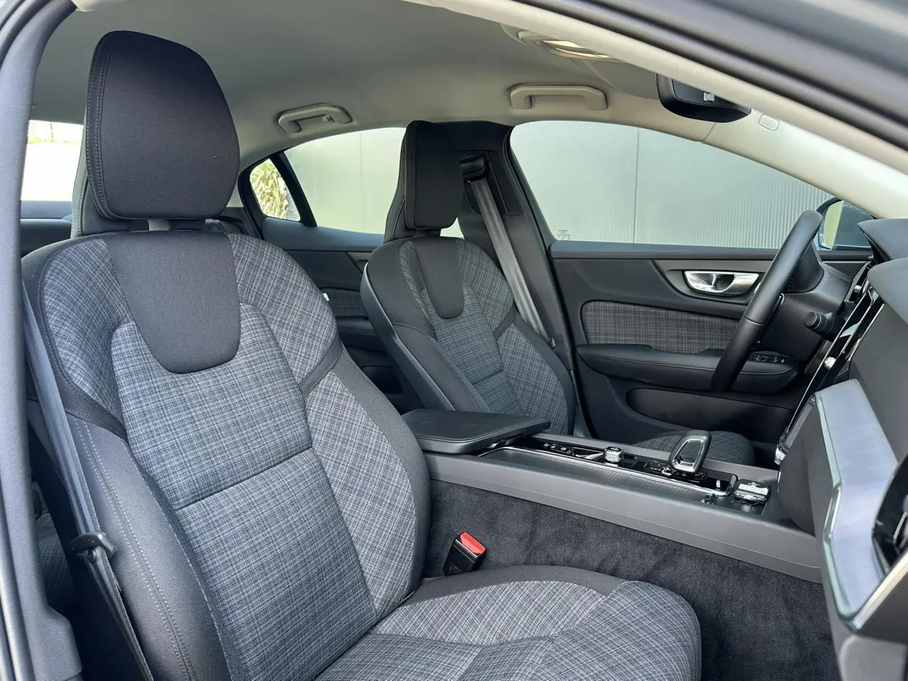Intérieur de la Volvo S60 B4 2024 vu côté droit, sièges tissu gris à motif tartan et console centrale moderne.