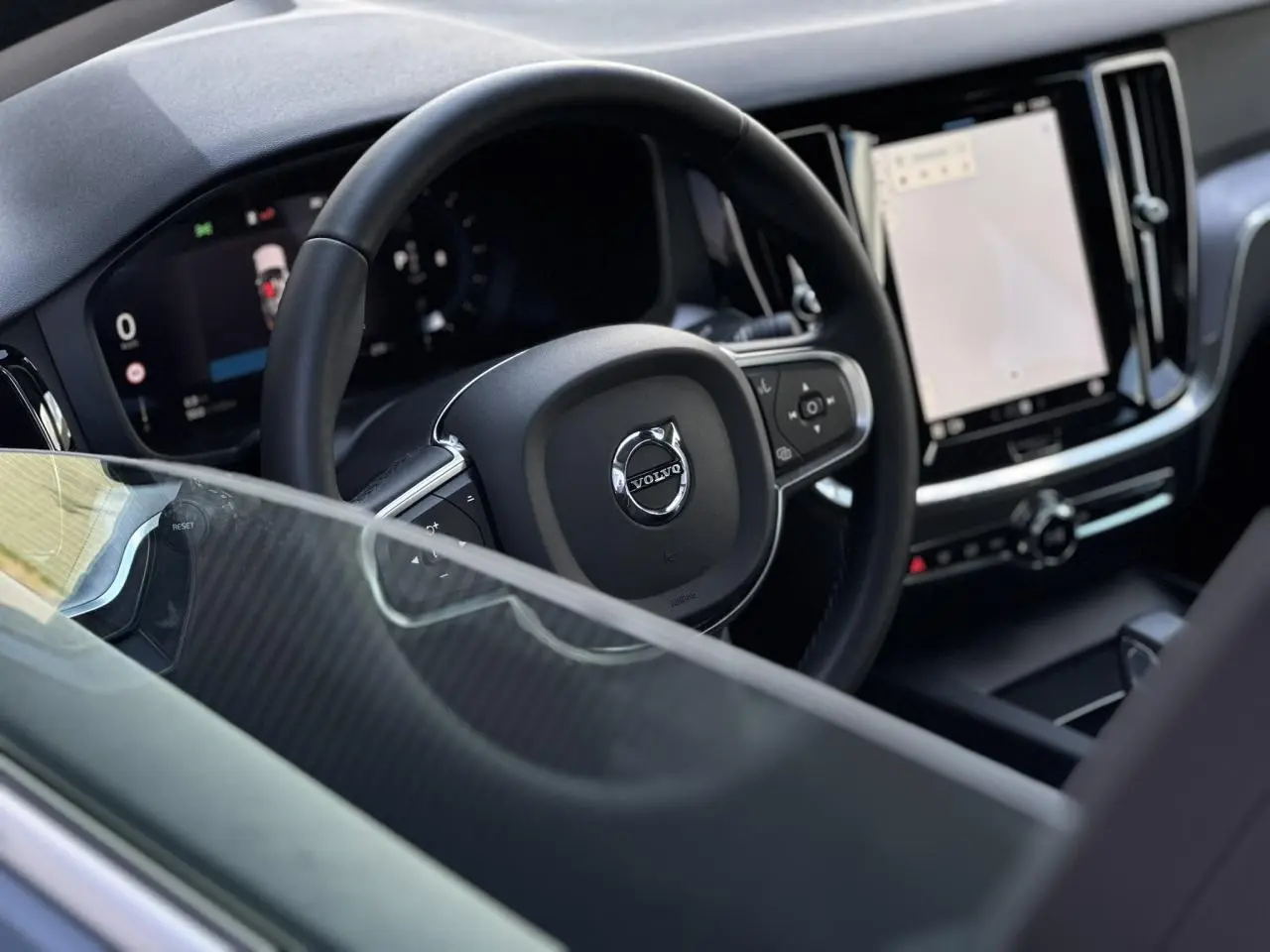 Vue intérieure centrée sur le volant noir et le tableau de bord numérique du Volvo S60 gris Thunder 2024.