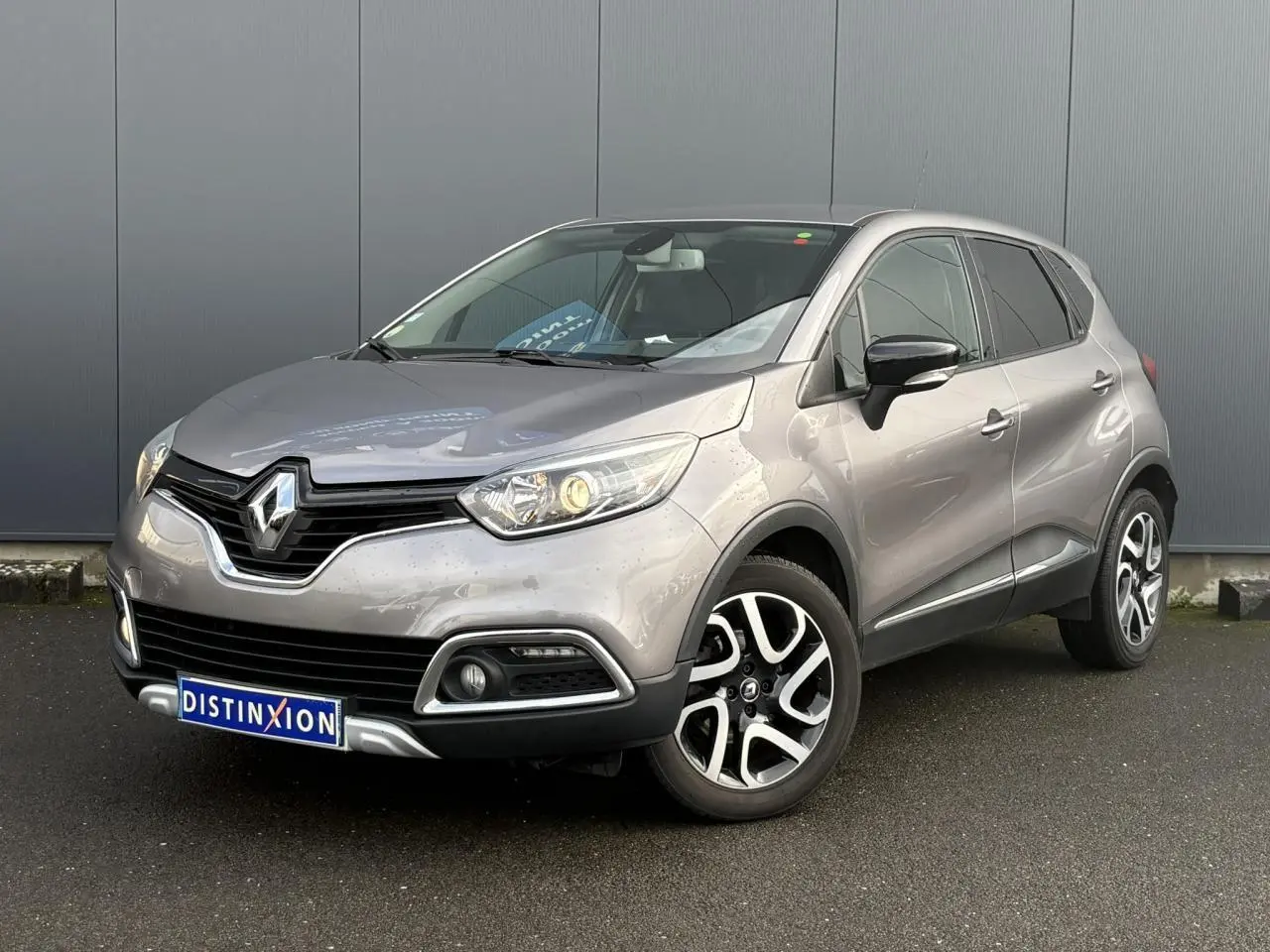 Renault Captur gris Cassiopée en 3/4 avant droit, avec jantes alliage noires et phares allumés.