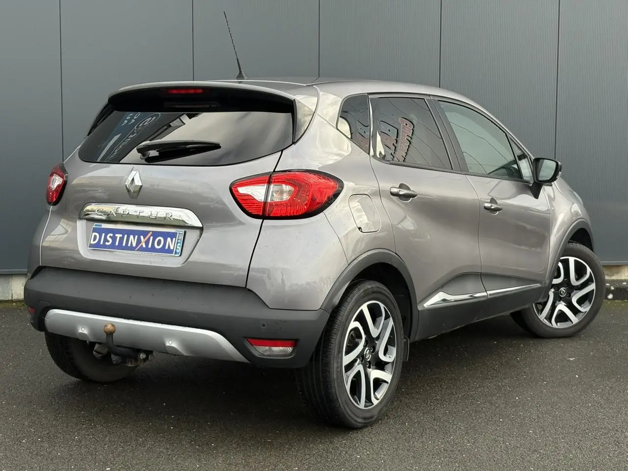 Vue 3/4 arrière droite d'un Renault Captur gris Cassiopée avec jantes alliage noires et attelage visible.