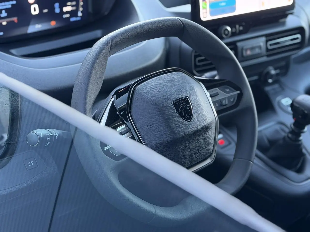 Vue rapprochée du volant multifonctions noir du Peugeot Partner 2026 avec tableau de bord et levier de vitesses manuelle.