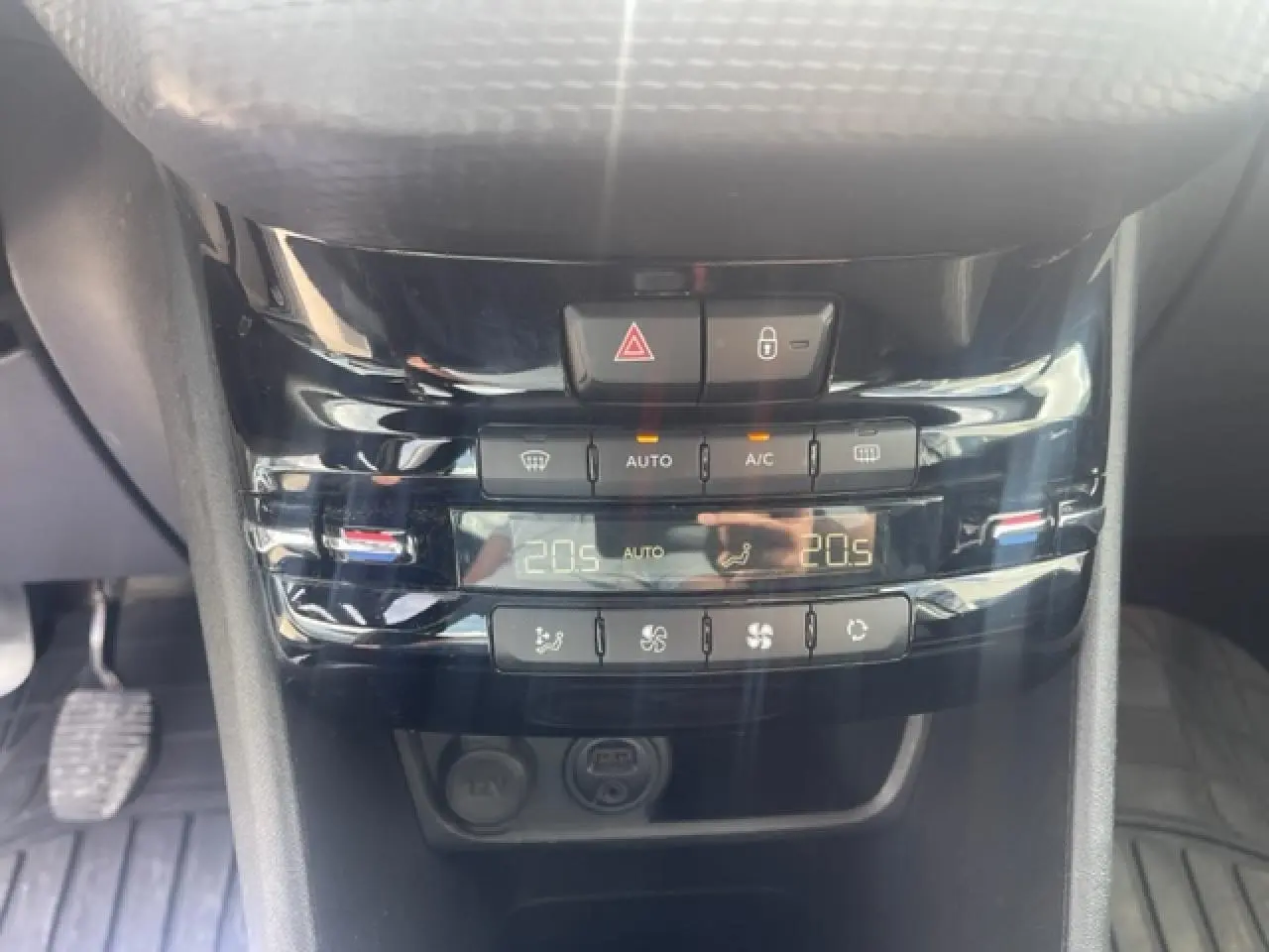 Gros plan sur la console centrale noire brillante de la Peugeot 208 avec commandes climatisation et affichage digital.