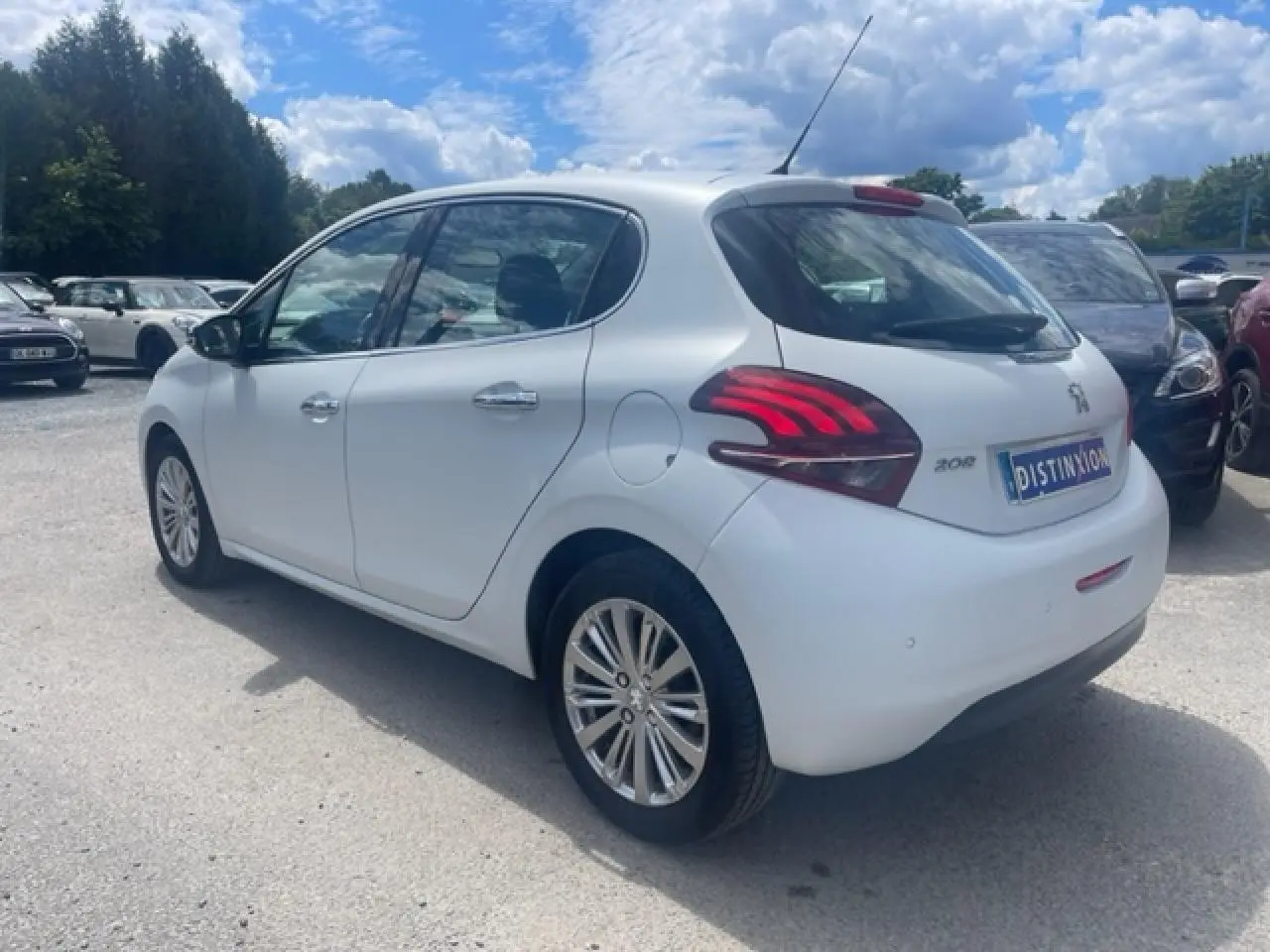 Peugeot 208 blanc perle vue 3/4 arrière droit, avec jantes alliage et feux arrière distinctifs rouges.