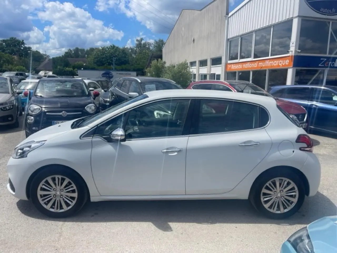 Profil côté gauche d'une Peugeot 208 blanc perle avec jantes alliage 16 pouces, stationnée en extérieur.