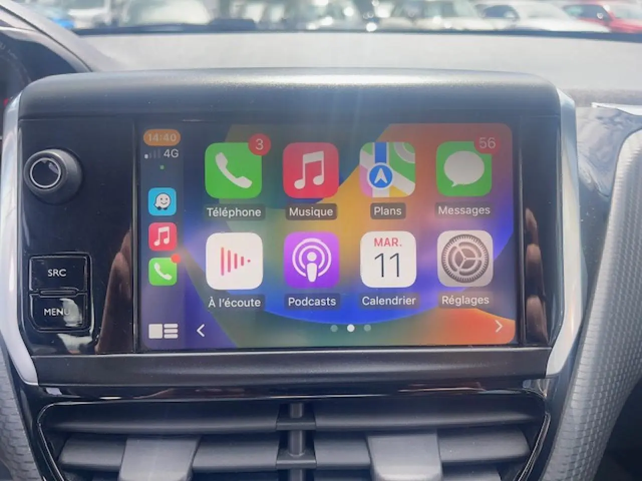 Écran tactile central avec interface CarPlay dans l’habitacle d’une Peugeot 208 blanche perle, vue de face rapprochée.