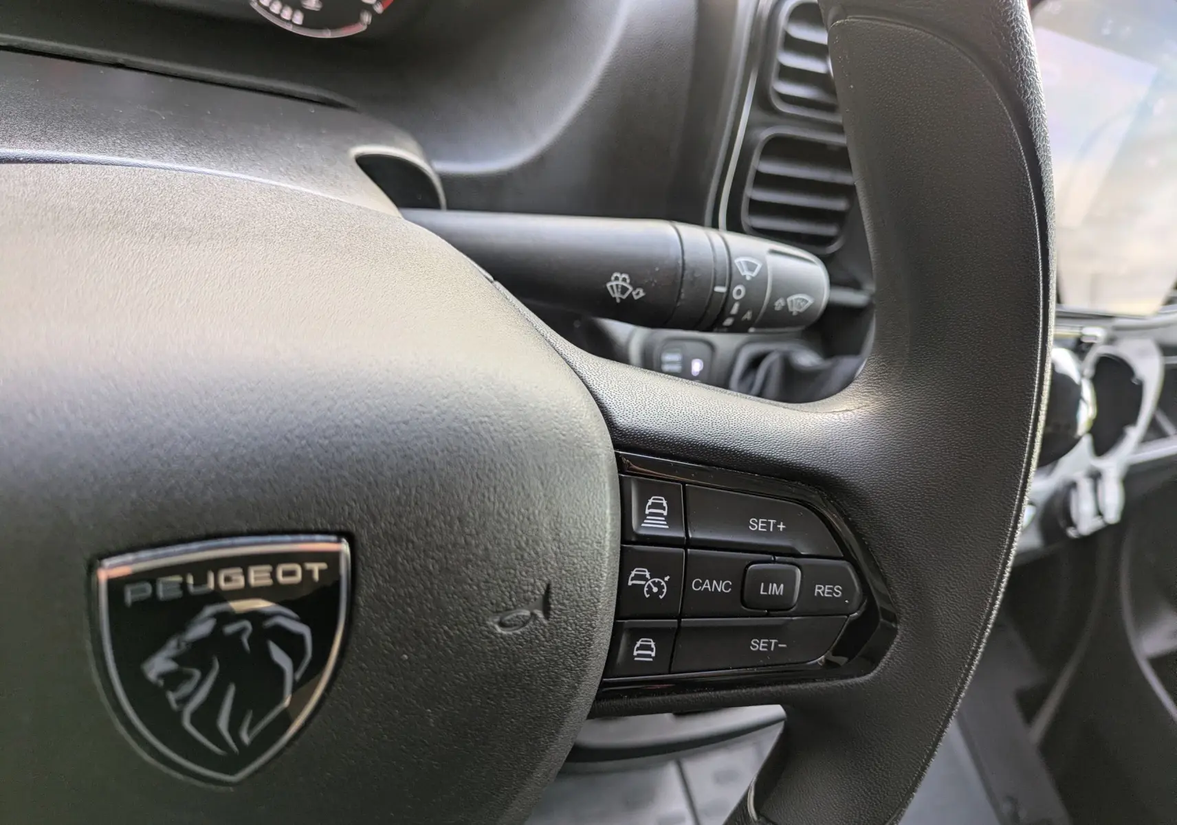 Gros plan sur le volant noir du Peugeot Boxer Fourgon blanc, avec commandes de régulateur de vitesse visibles à droite.
