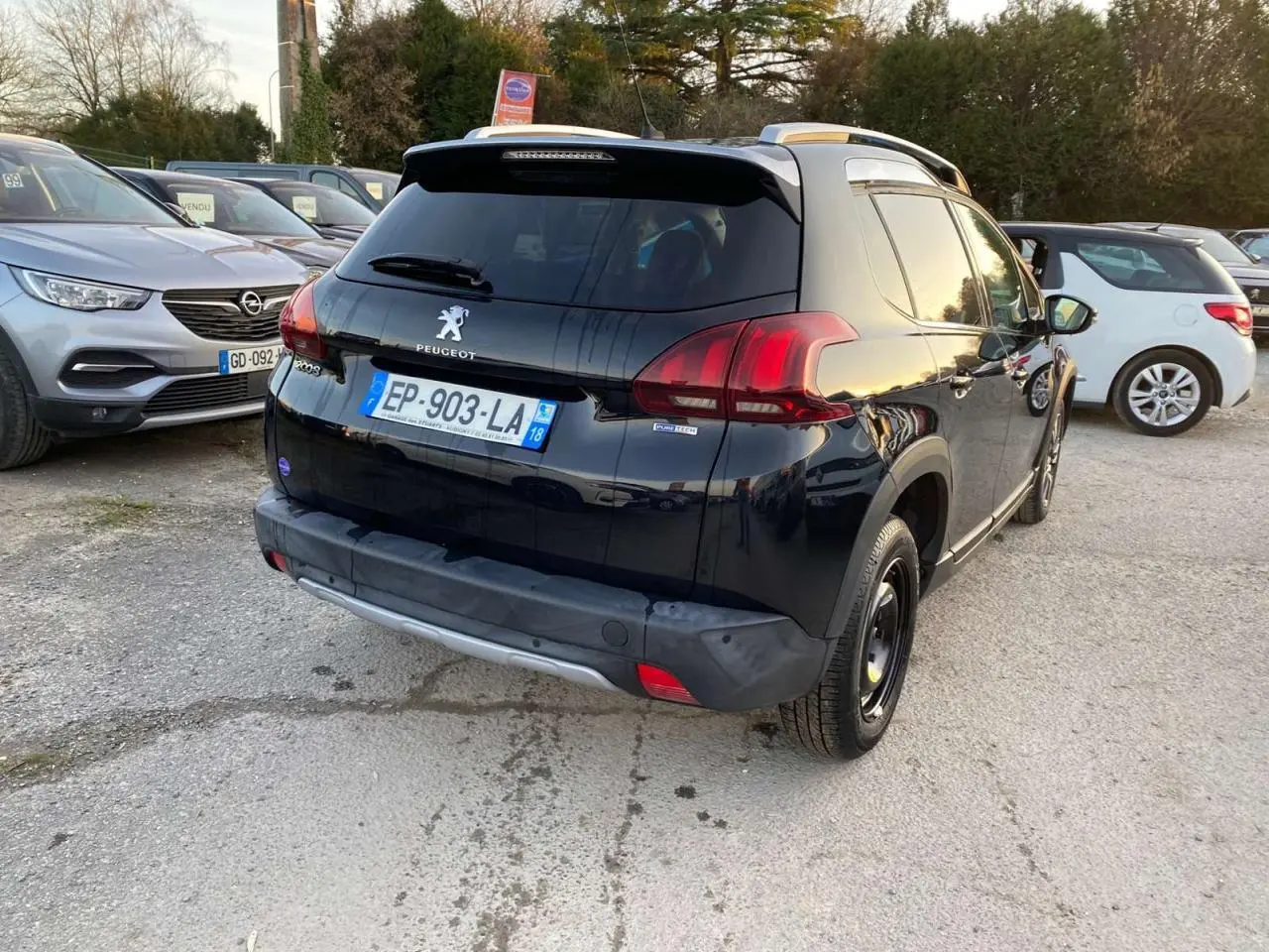 Peugeot 2008 noir Perla Nera vue 3/4 arrière droit, avec feux arrière rouges et toit avec barres de toit.