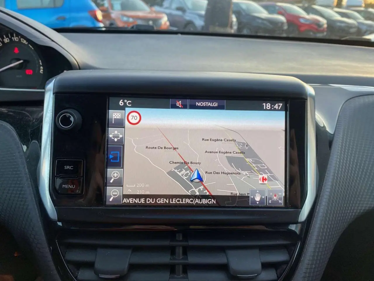 Vue intérieure centrée sur l'écran tactile du GPS du Peugeot 2008, avec tableau de bord et voitures en arrière-plan.