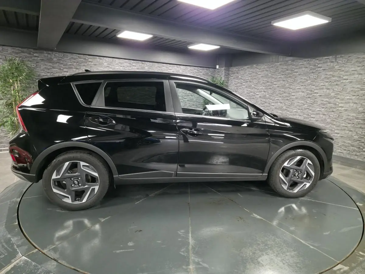 Vue de profil côté gauche d'un Hyundai Bayon noir 2025 avec jantes alliage 17 pouces dans un showroom intérieur.