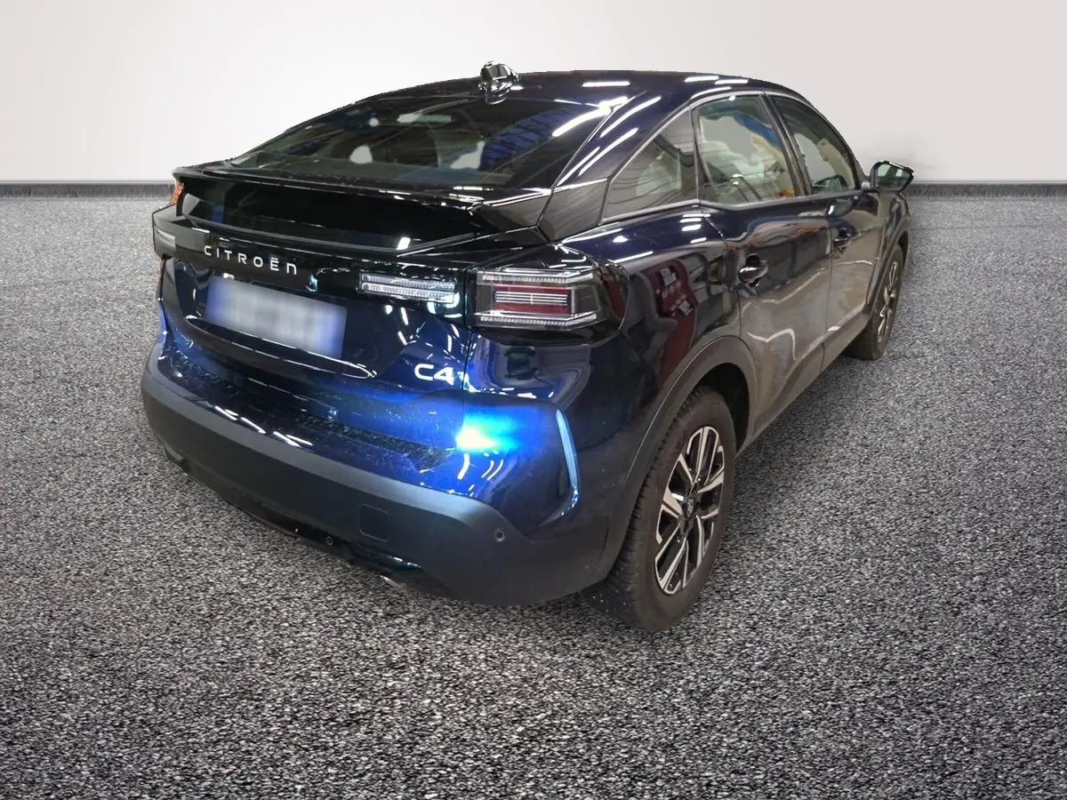 Vue 3/4 arrière droite d'une Citroën C4 hybride 2025 bleu foncé avec feux arrière LED et spoiler de coffre.
