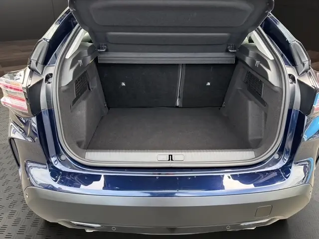 Vue arrière du coffre ouvert d'une Citroën C4 hybride 2025 bleu, montrant l'espace de chargement et la finition intérieure noire.