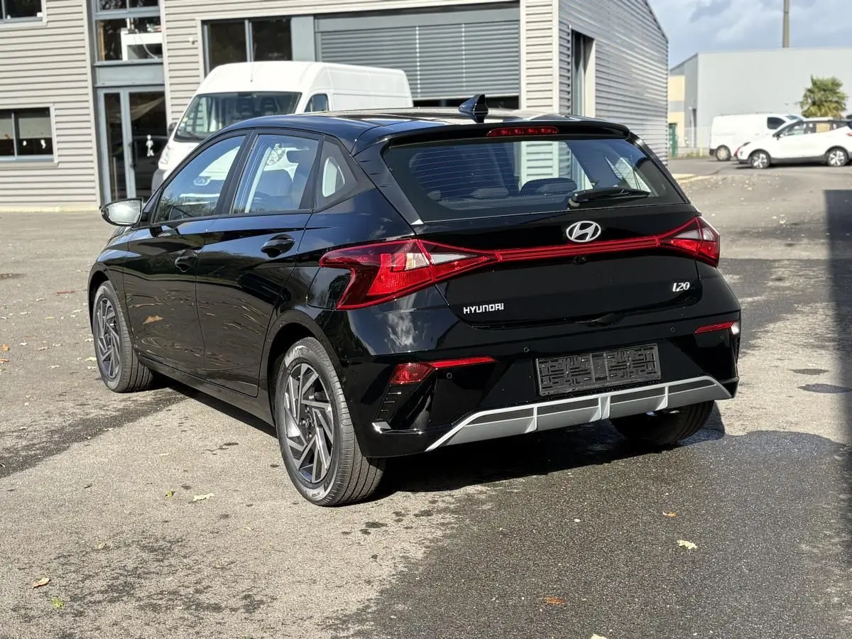 Vue 3/4 arrière droite d'une Hyundai i20 noire métal 2026 avec feux arrière reliés et jantes alliage distinctives.