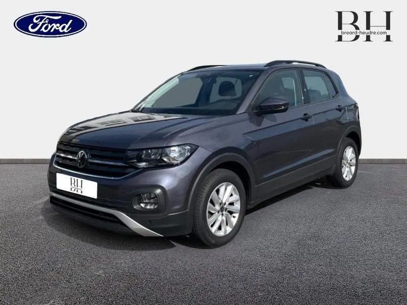 Volkswagen T-Cross gris cendré métallisé en 3/4 avant droit avec barres de toit et jantes alu visibles.