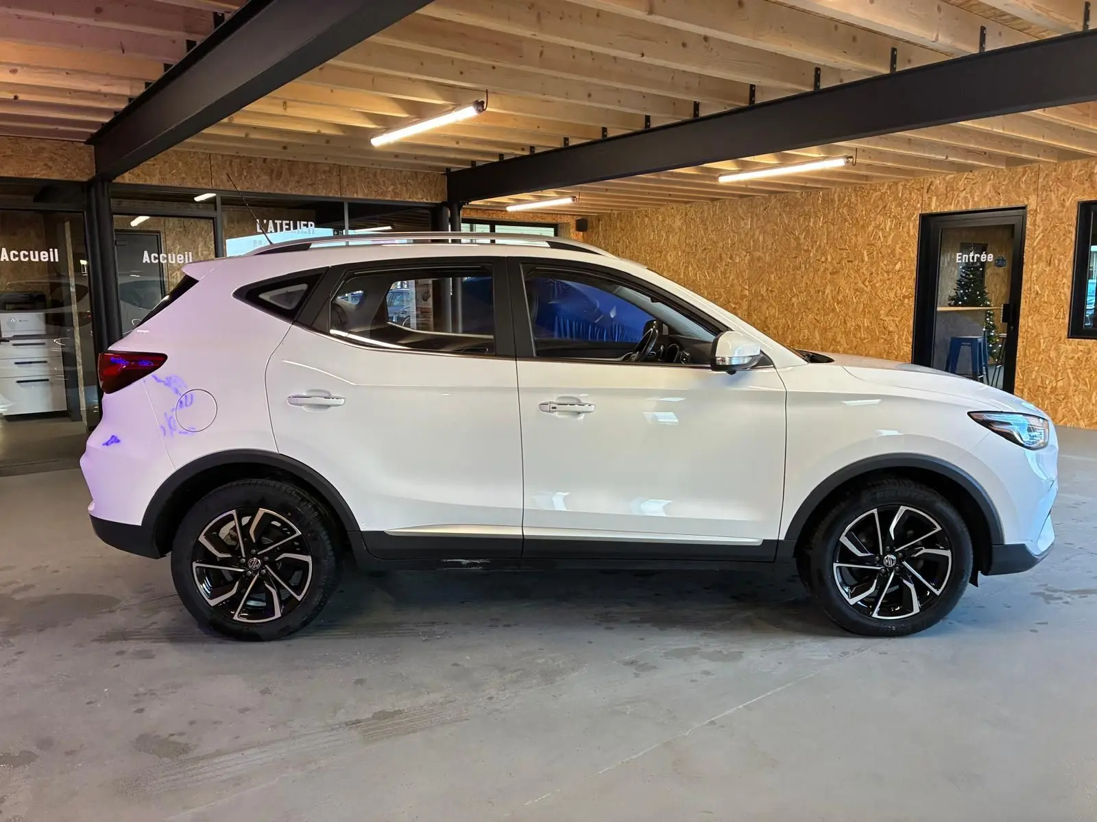 Vue de profil côté gauche du SUV blanc MG ZS 2022 avec jantes alliage noires et intérieur visible.
