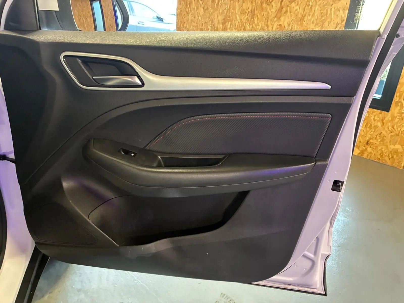 Vue intérieure de la porte avant gauche du MG ZS blanc, avec garniture noire et surpiqûres rouges visibles.