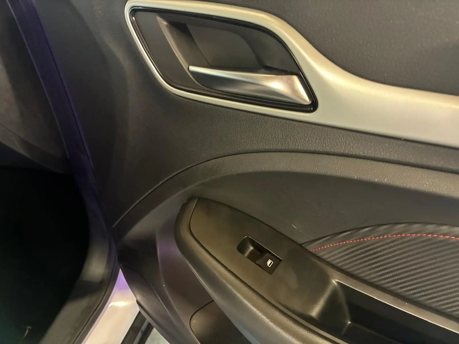 Gros plan sur la poignée intérieure et le panneau de porte côté gauche du MG ZS blanc, avec surpiqûres rouges décoratives.