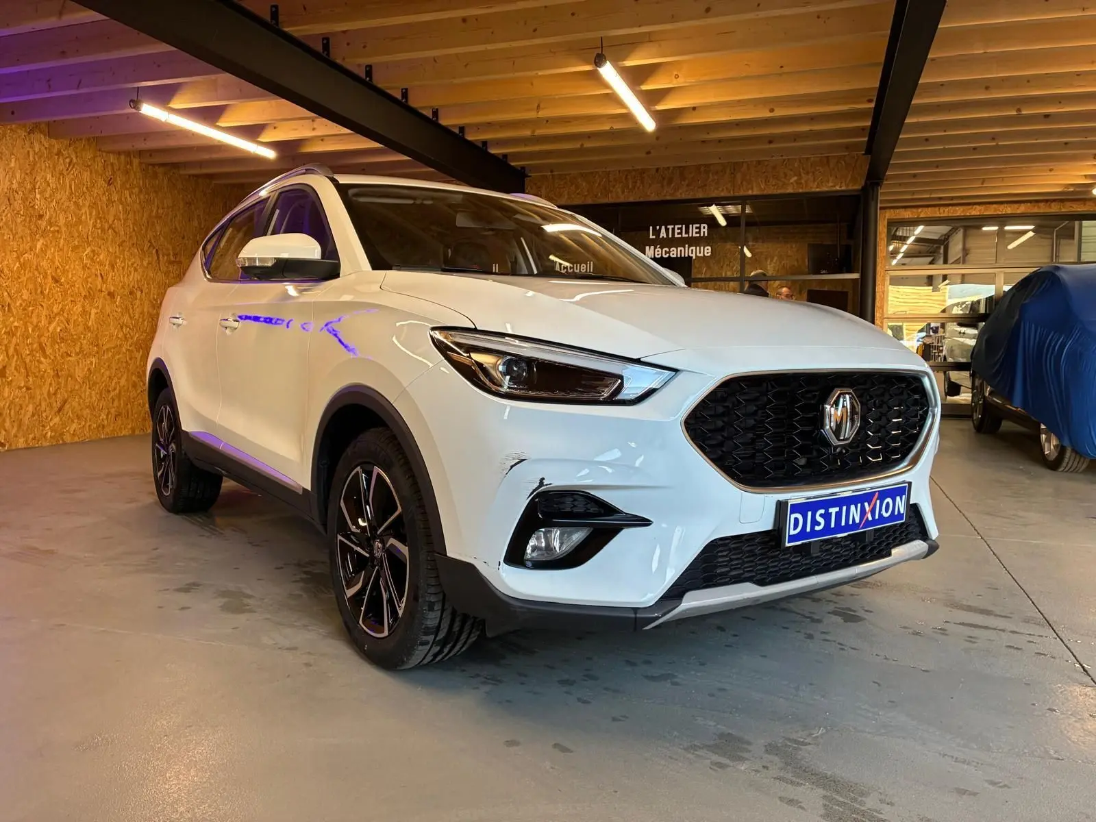 Vue 3/4 avant droite du MG ZS blanc 2022 dans un garage, avec calandre noire et jantes alliage noires.