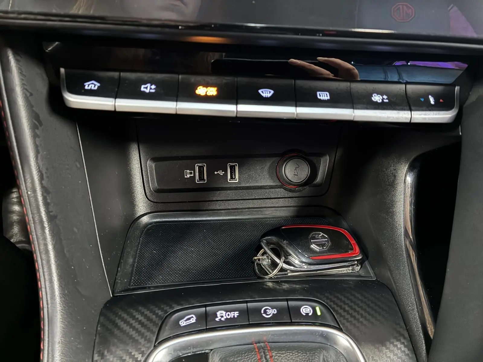 Gros plan sur la console centrale noire avec touches de climatisation, ports USB et clé MG ZS blanche posée.