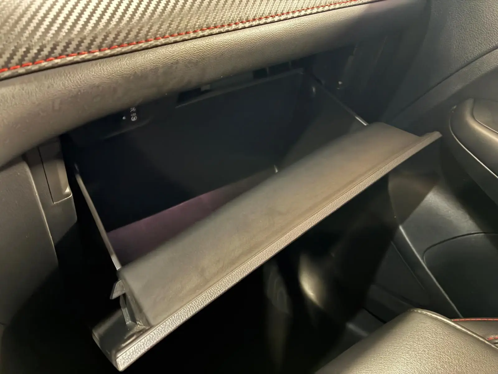Vue intérieure du vide-poche ouvert côté passager du MG ZS blanc, avec finition cuir noir et surpiqûres rouges.