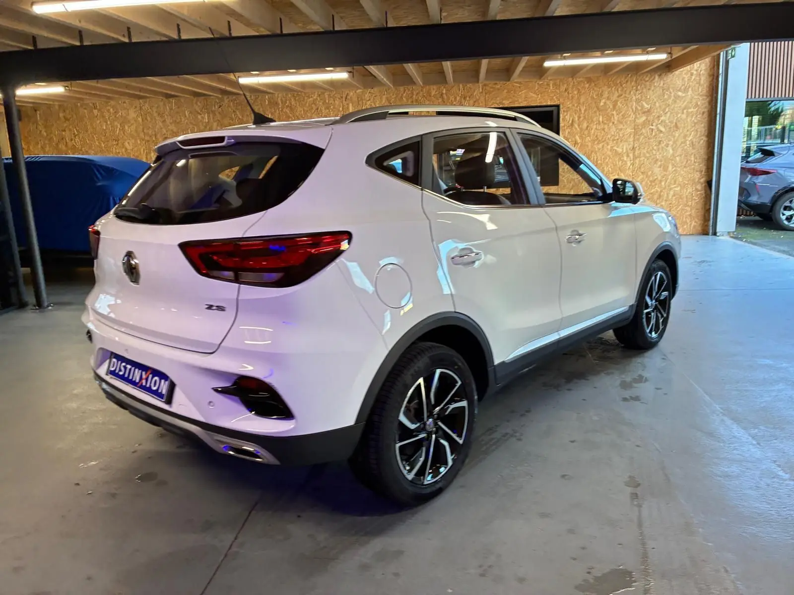 Vue 3/4 arrière droite du SUV blanc MG ZS 2022, avec jantes noires et détails chromés, stationné en intérieur.