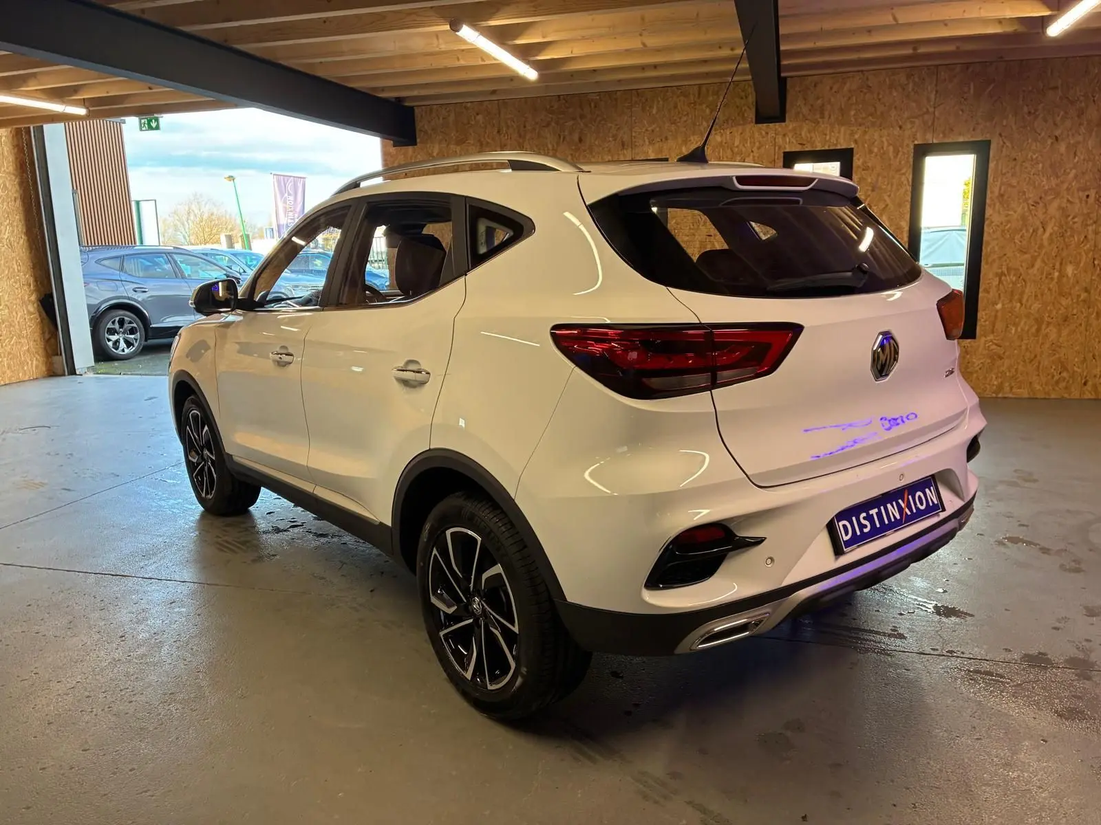 Vue 3/4 arrière droite d’un MG ZS blanc 2022 dans un garage, avec jantes noires et détails chromés.