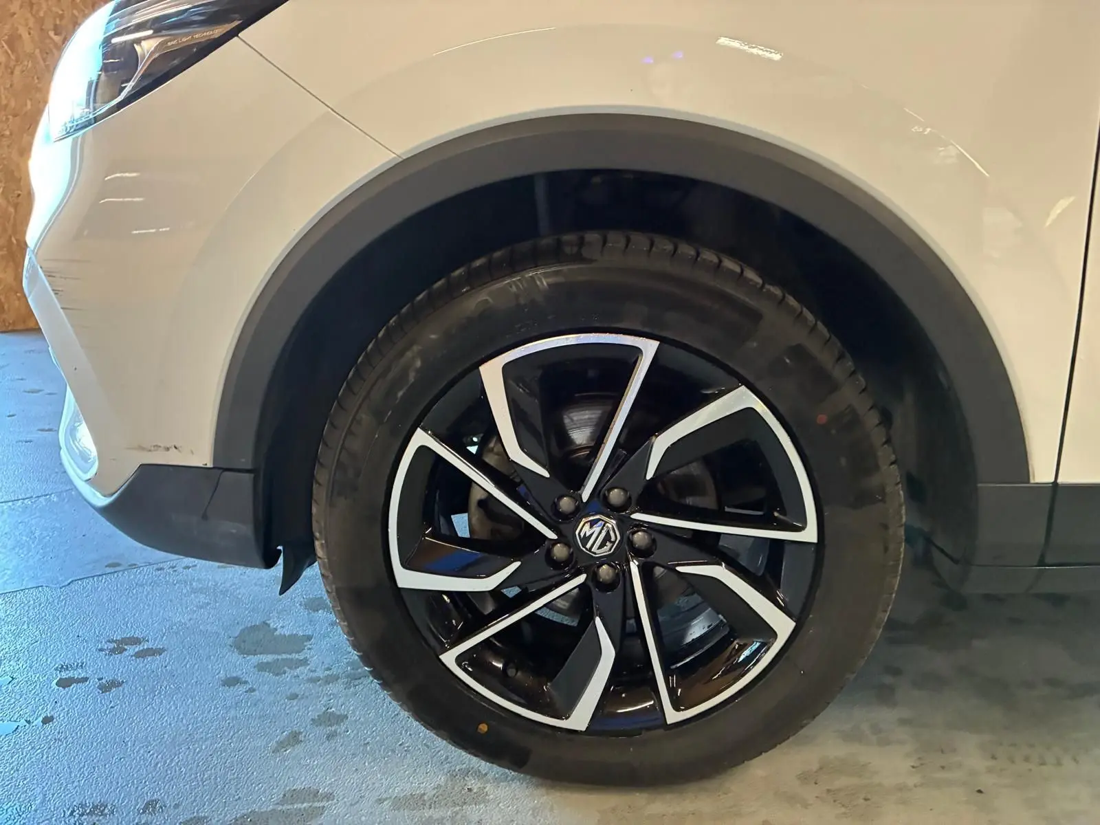 Gros plan sur la roue avant gauche noire et argentée du MG ZS blanc, mettant en valeur la jante au design moderne.