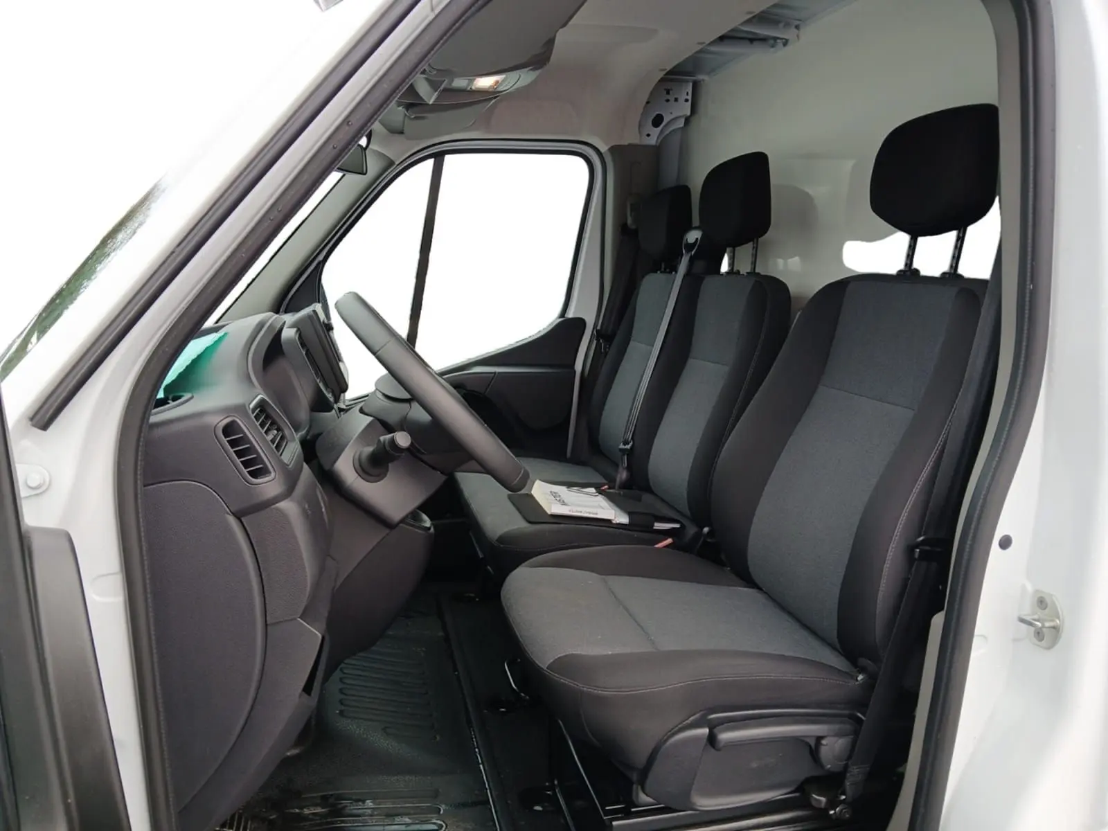 Vue intérieure côté conducteur du Renault Master blanc 2023, montrant les sièges avant en tissu gris et noir.