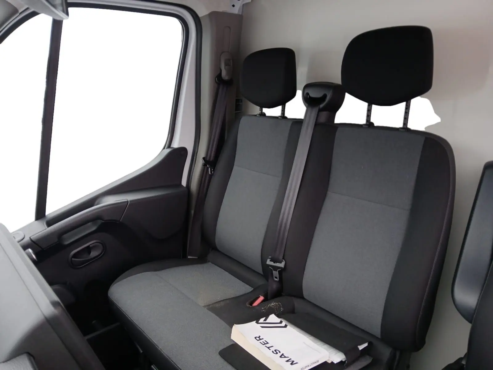 Vue intérieure côté passager montrant la banquette grise et noire du Renault Master 2023 avec un manuel posé dessus.