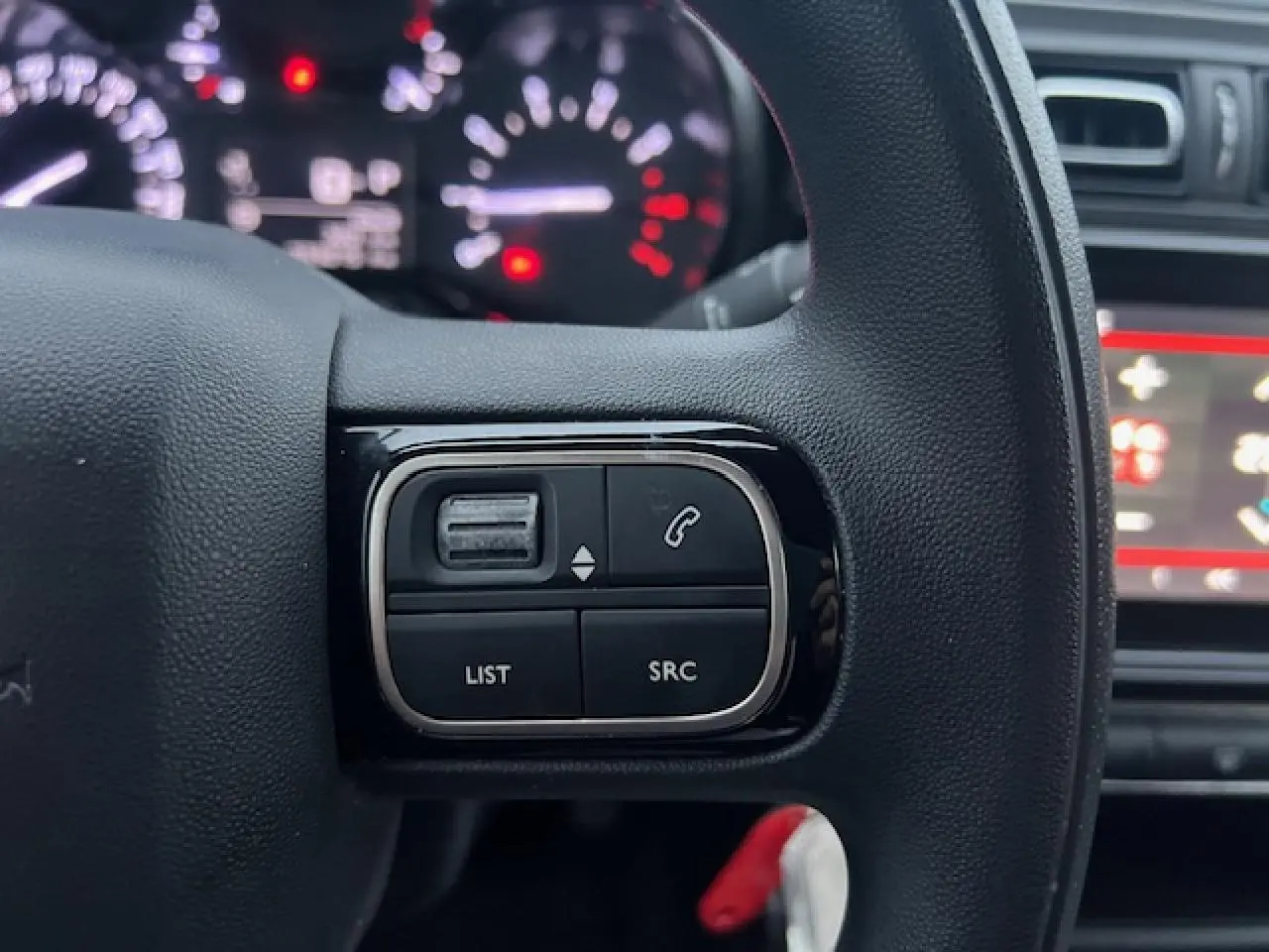 Gros plan sur les commandes audio au volant à gauche du Citroën C3 Shine 2023, intérieur noir avec tableau de bord flou.