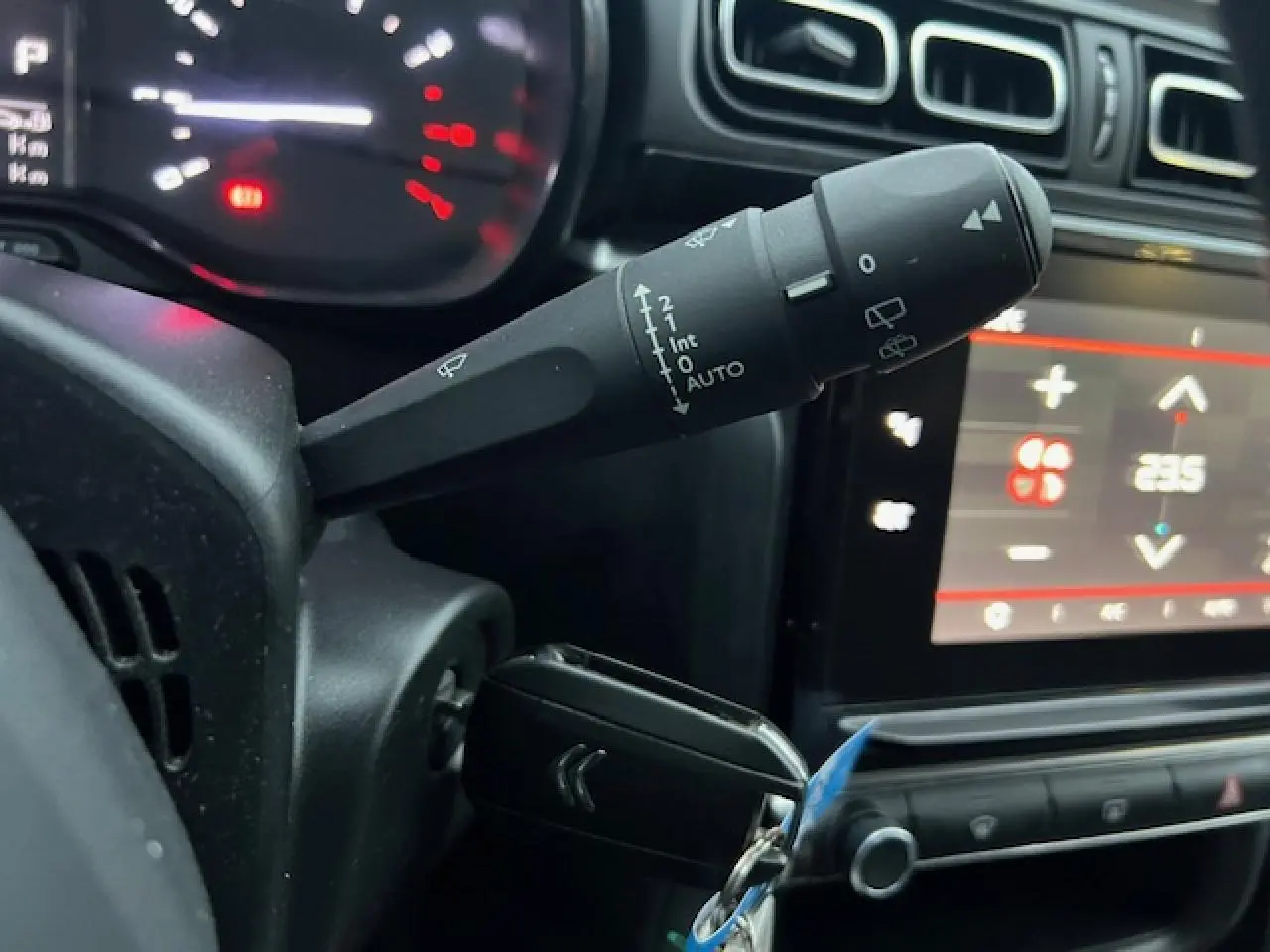Gros plan sur la commande d’essuie-glace et le tableau de bord numérique d’une Citroën C3 Shine 2023 essence, intérieur noir.