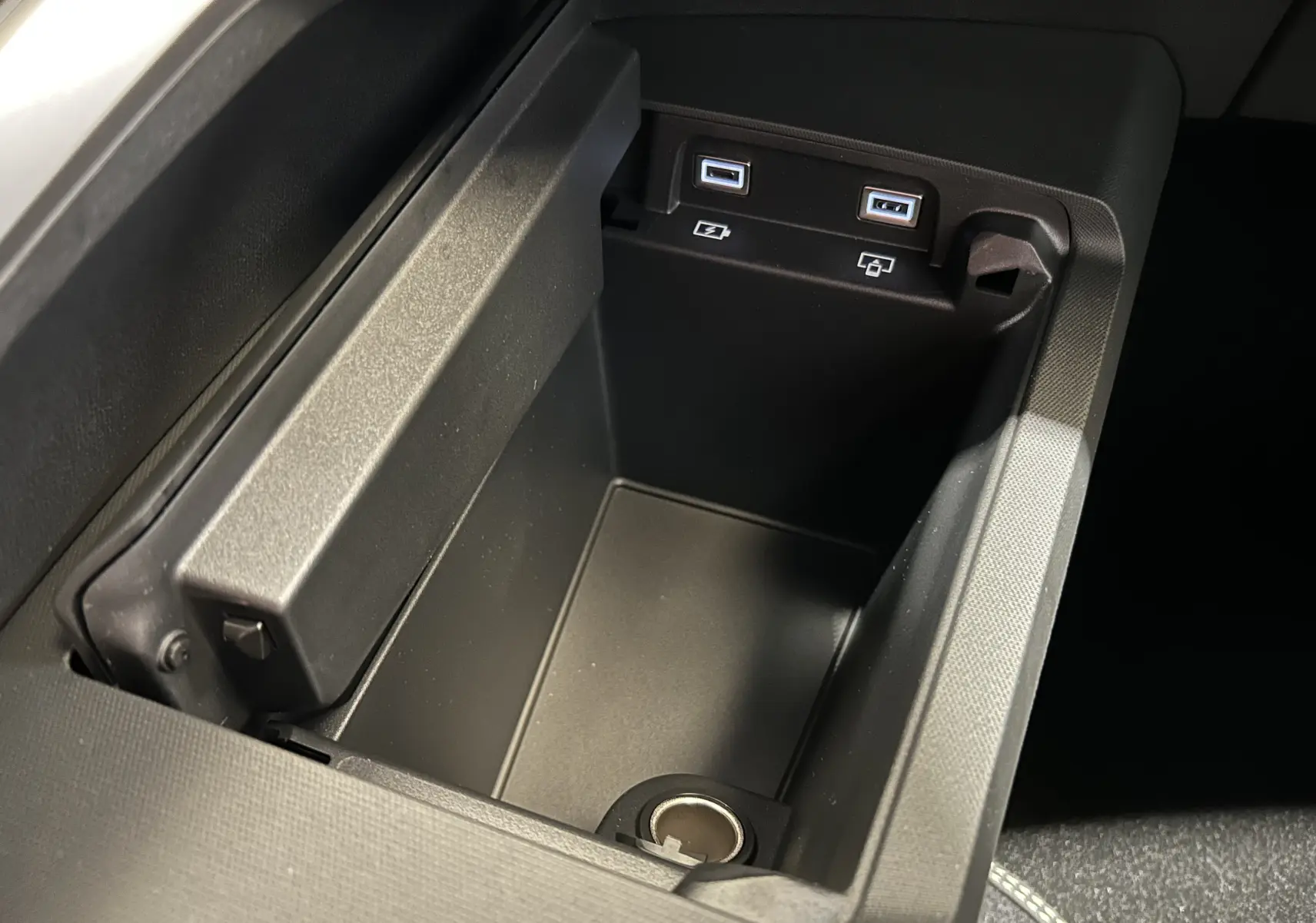Gros plan sur la console centrale noire du Peugeot 3008 Hybrid avec ports USB et prise 12V visibles.