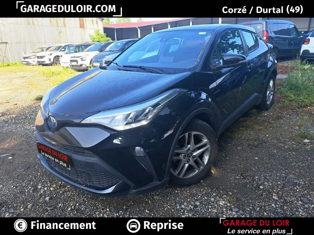 Vue 3/4 avant d'une Toyota C-HR 1.8 Hybride noire avec jantes alliage, garée sur un sol gravillonné.