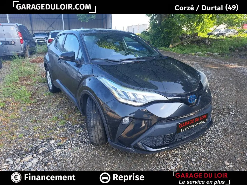 Toyota C-HR noir vue 3/4 avant droit sur terrain gravillonné avec calandre et phares LED distinctifs.
