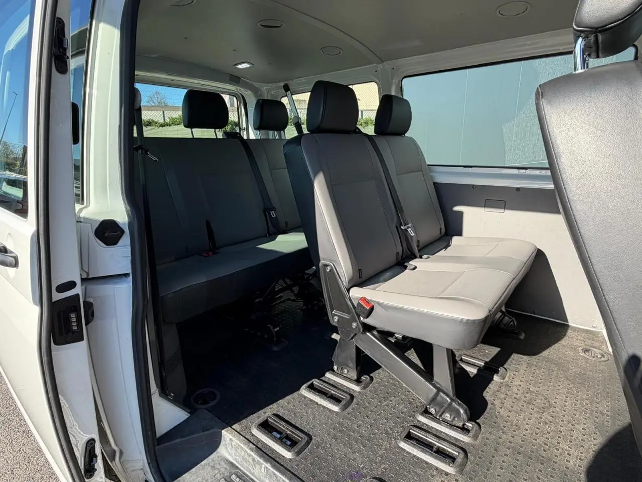 Vue intérieure côté droit du Volkswagen Transporter T6 Minibus blanc, montrant les sièges passagers en rangées.