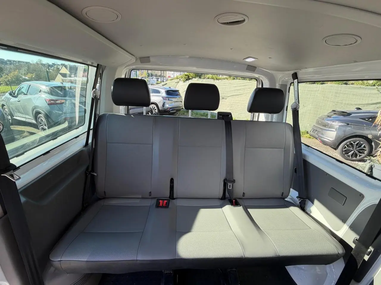 Banquette arrière grise vue de face à l'intérieur du Volkswagen Transporter T6 Minibus blanc, avec ceintures de sécurité visibles.