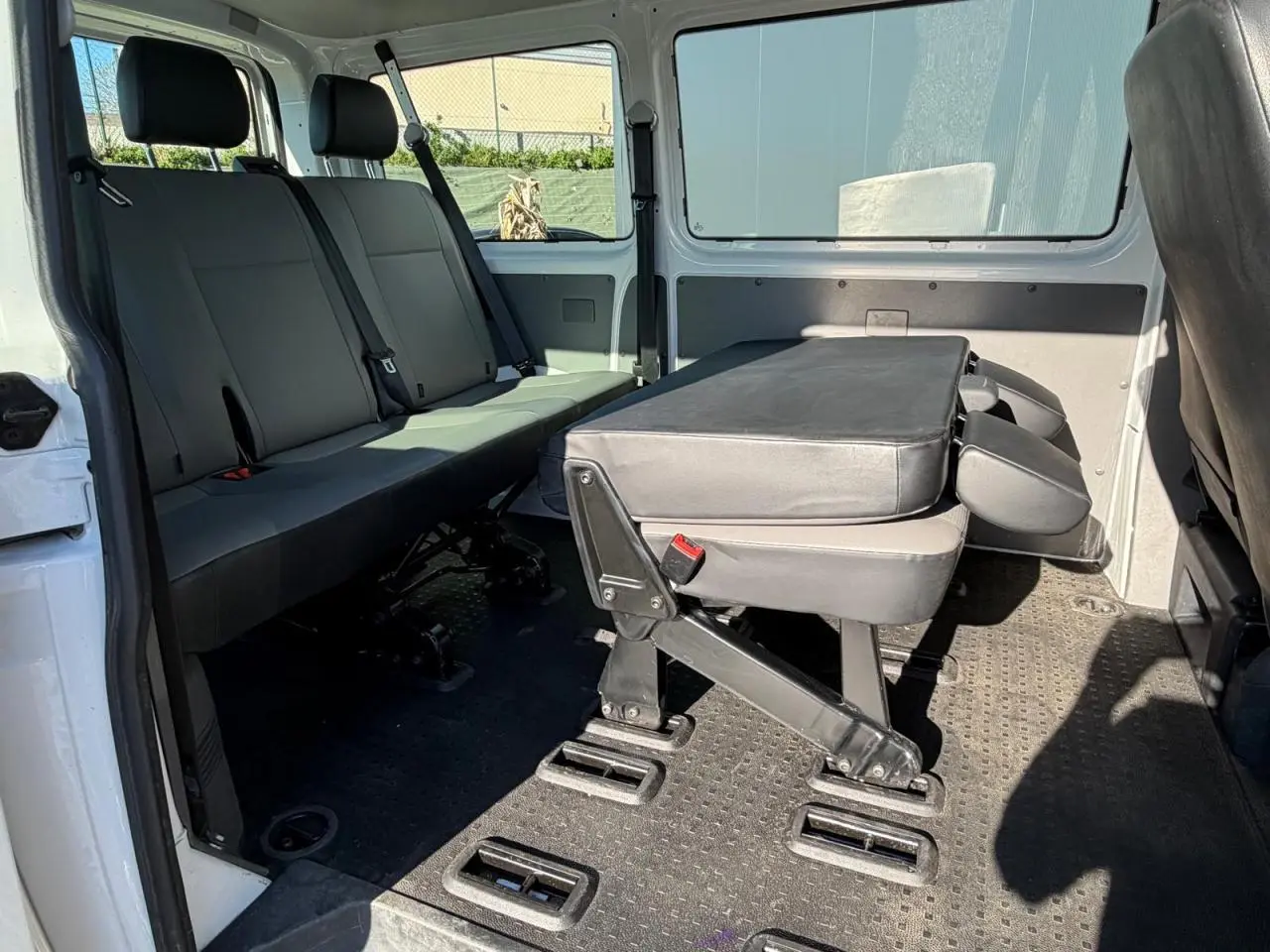 Vue intérieure côté droit du Volkswagen Transporter T6 Minibus blanc, montrant les sièges arrière et une banquette rabattue.